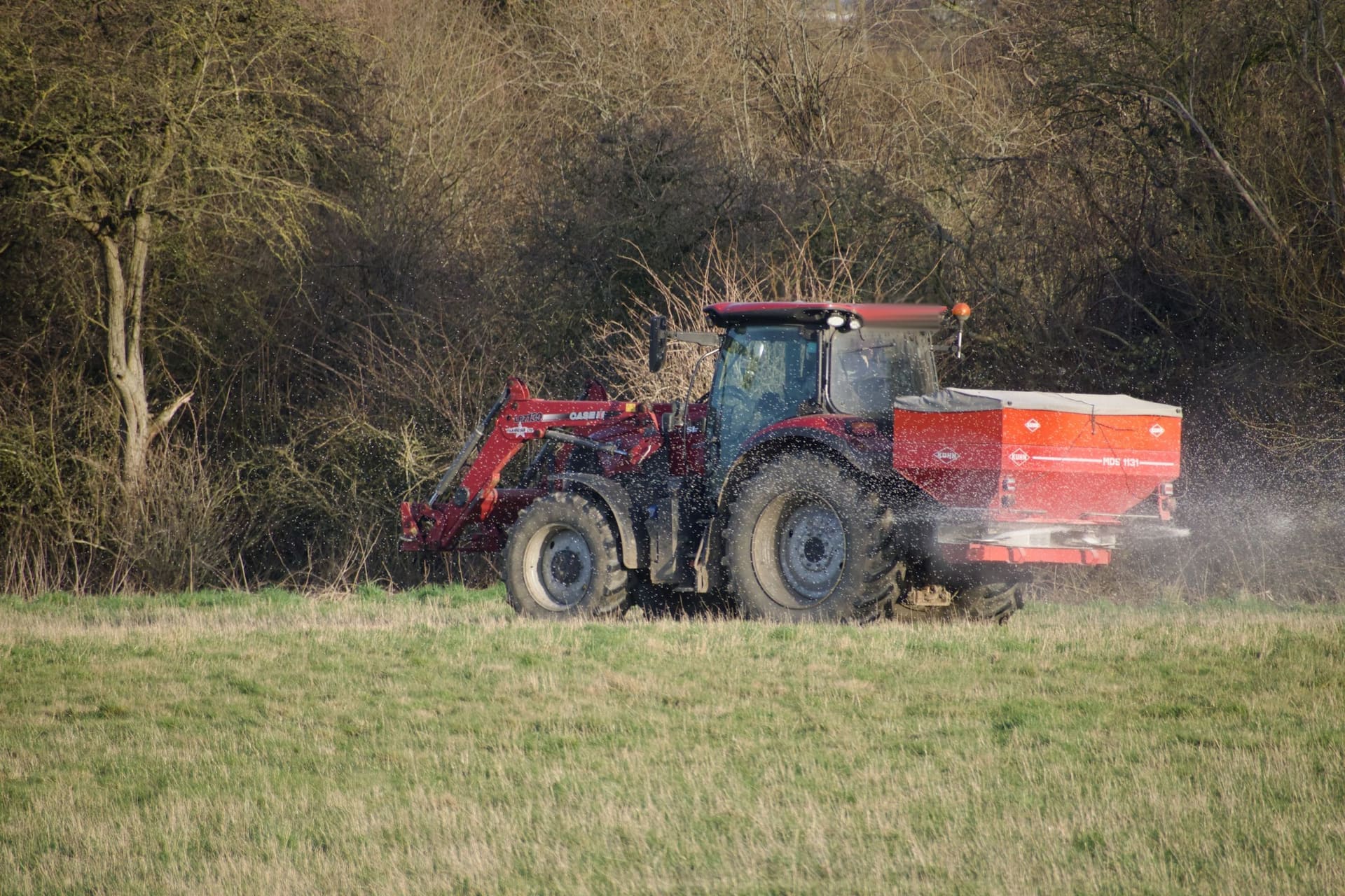 Traktor s rozmetadlom rozhadzuje granulované hnojivo na jarnom poli
